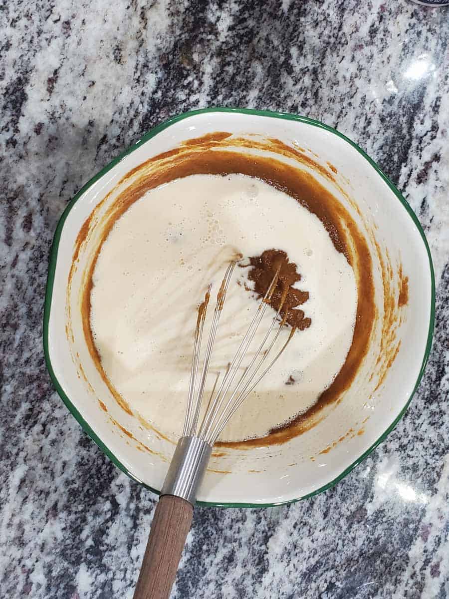 White mixing bowl with a green rim and a whisk in the process of making mini pumpkin pie filling.