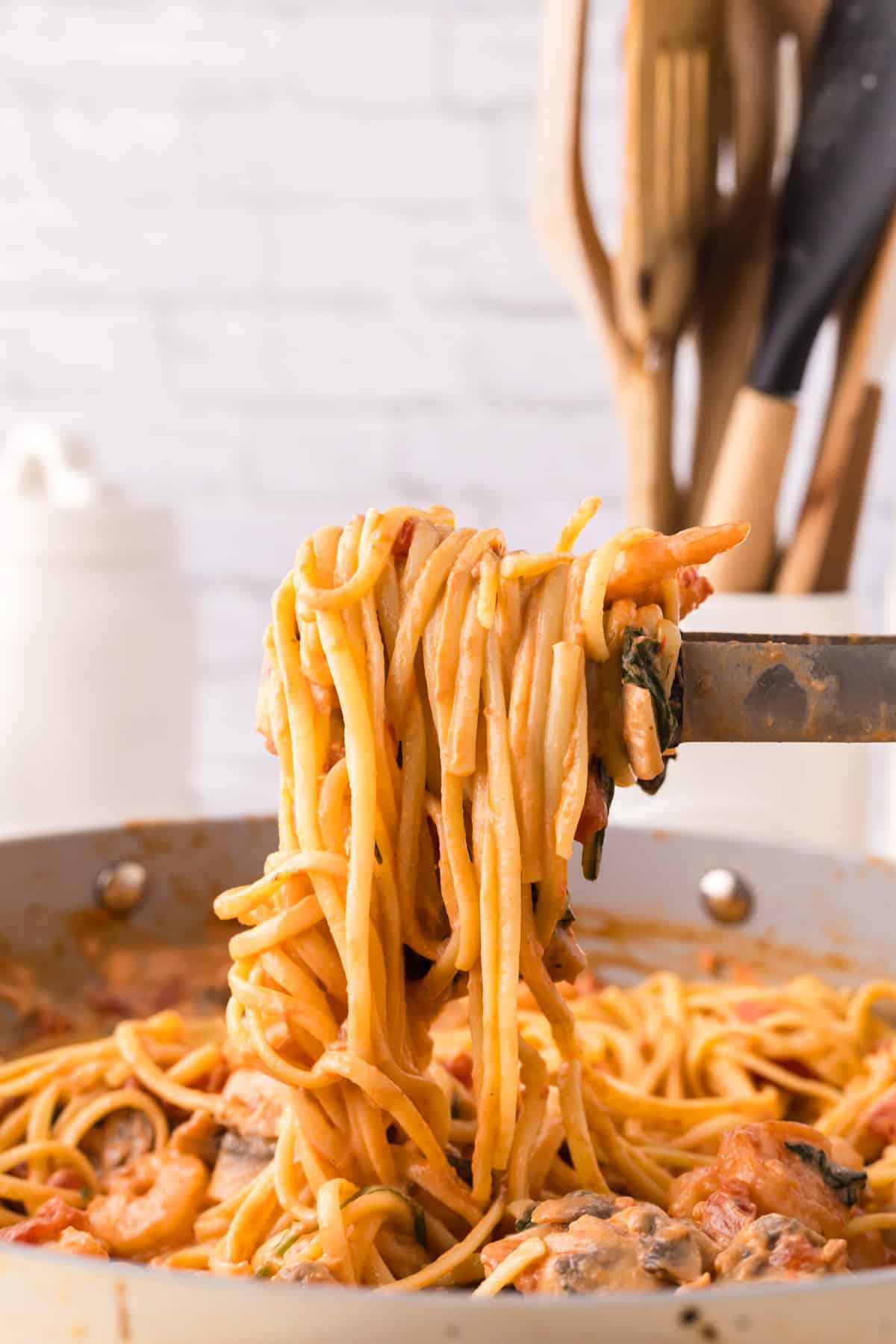 linguini rosa with shrimp in the pot held with tongs.