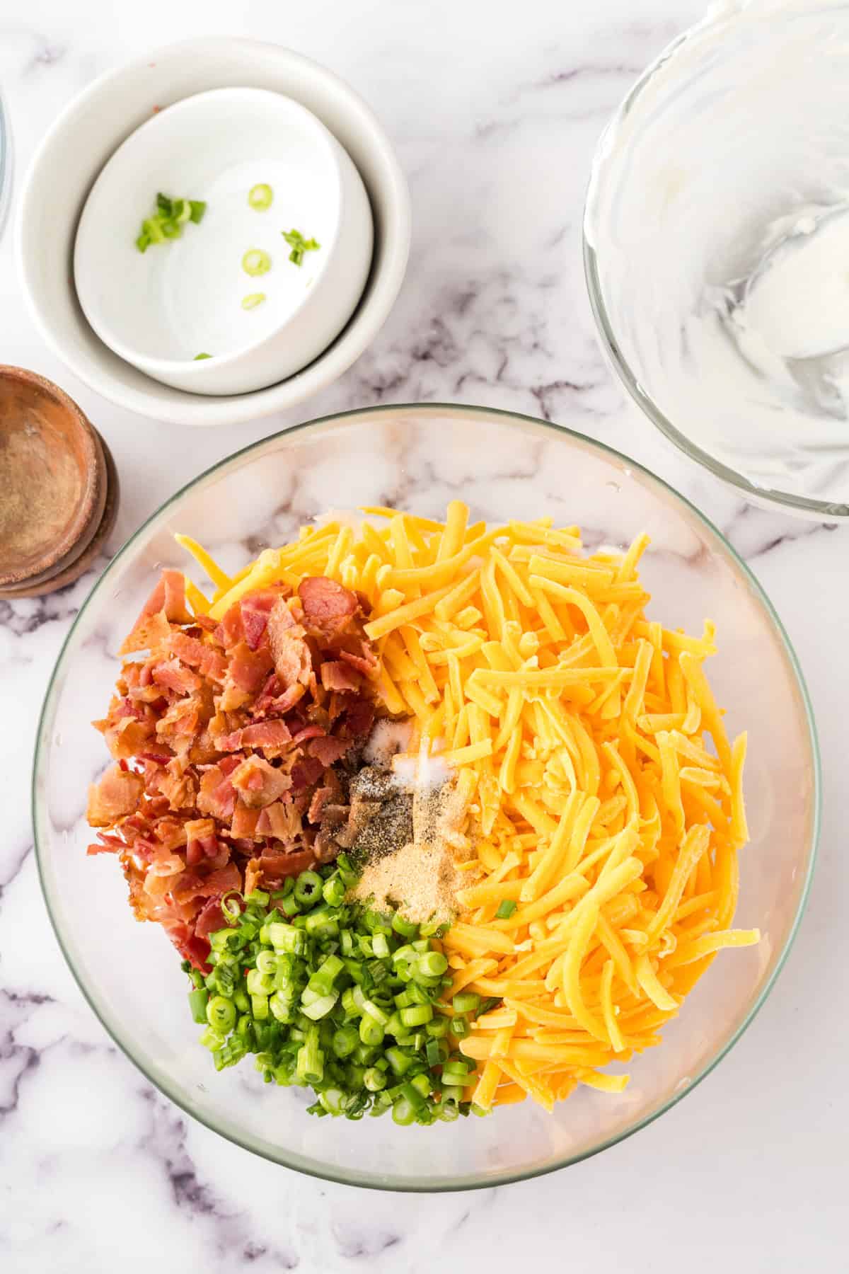 loaded baked potato dip in a clear mixing bowl in progress.