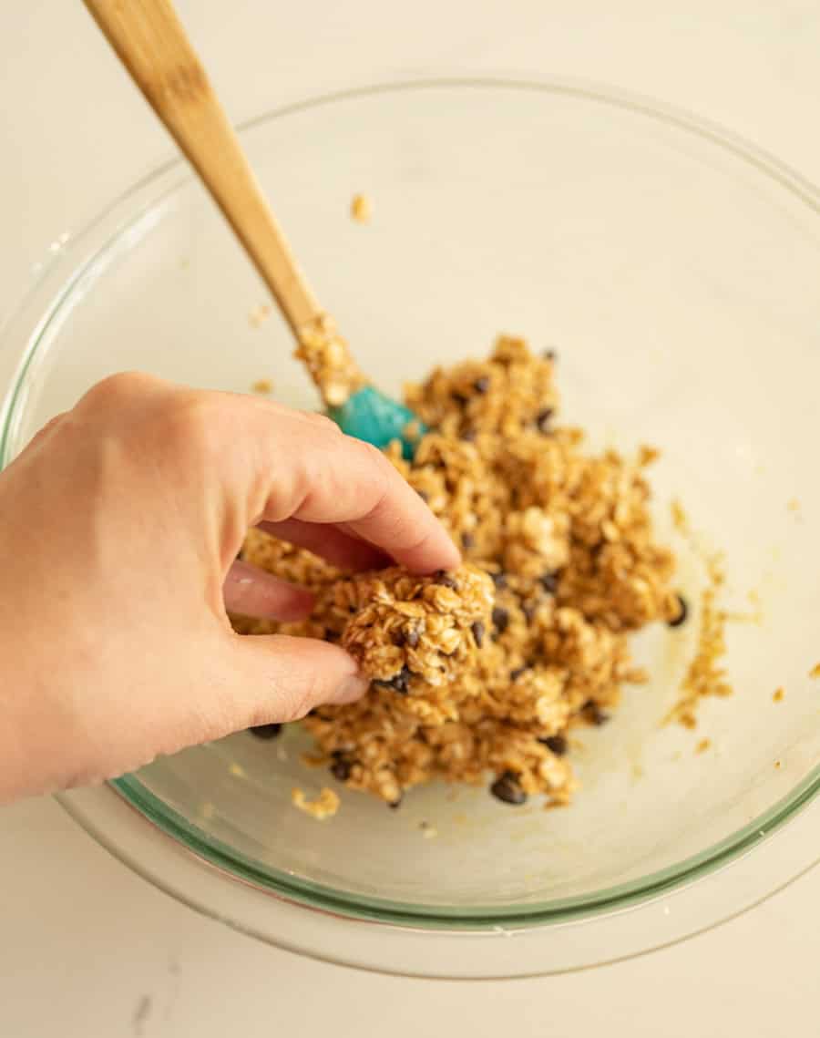 A hand forming some of the no-bake oatmeal energy ball dough into a bal.