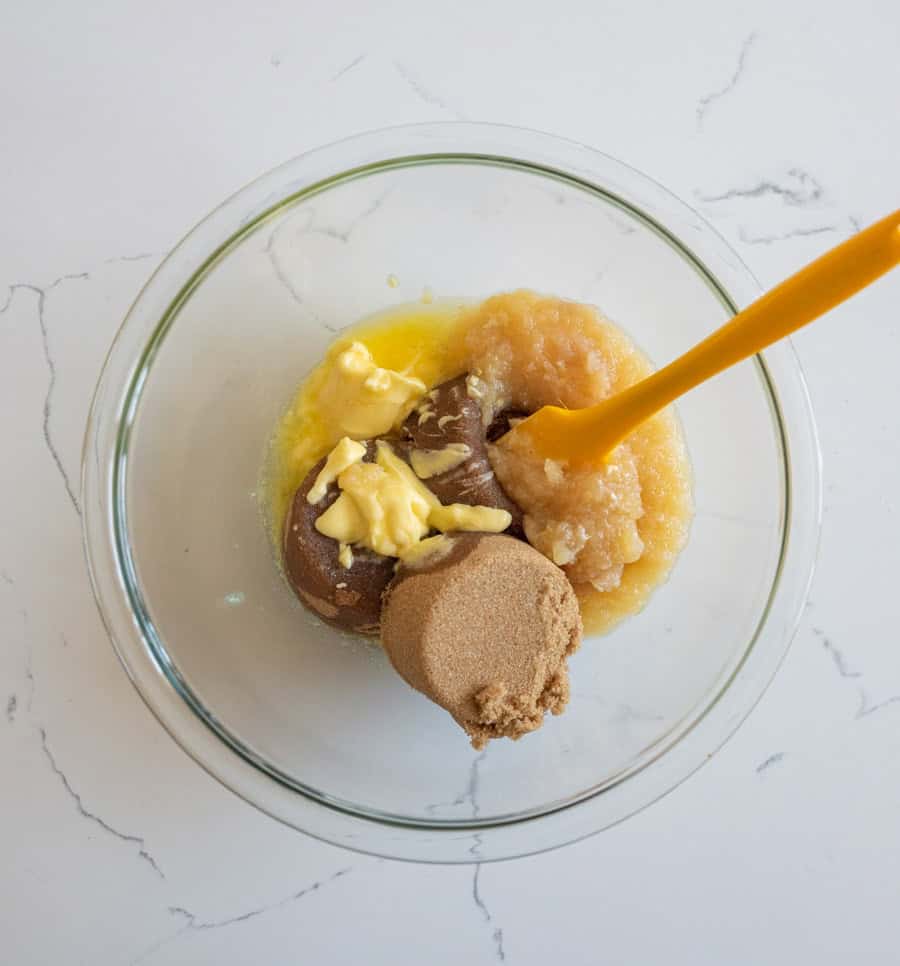 Butter, applesauce, and brown sugar in a clear glass bowl on a white counter.