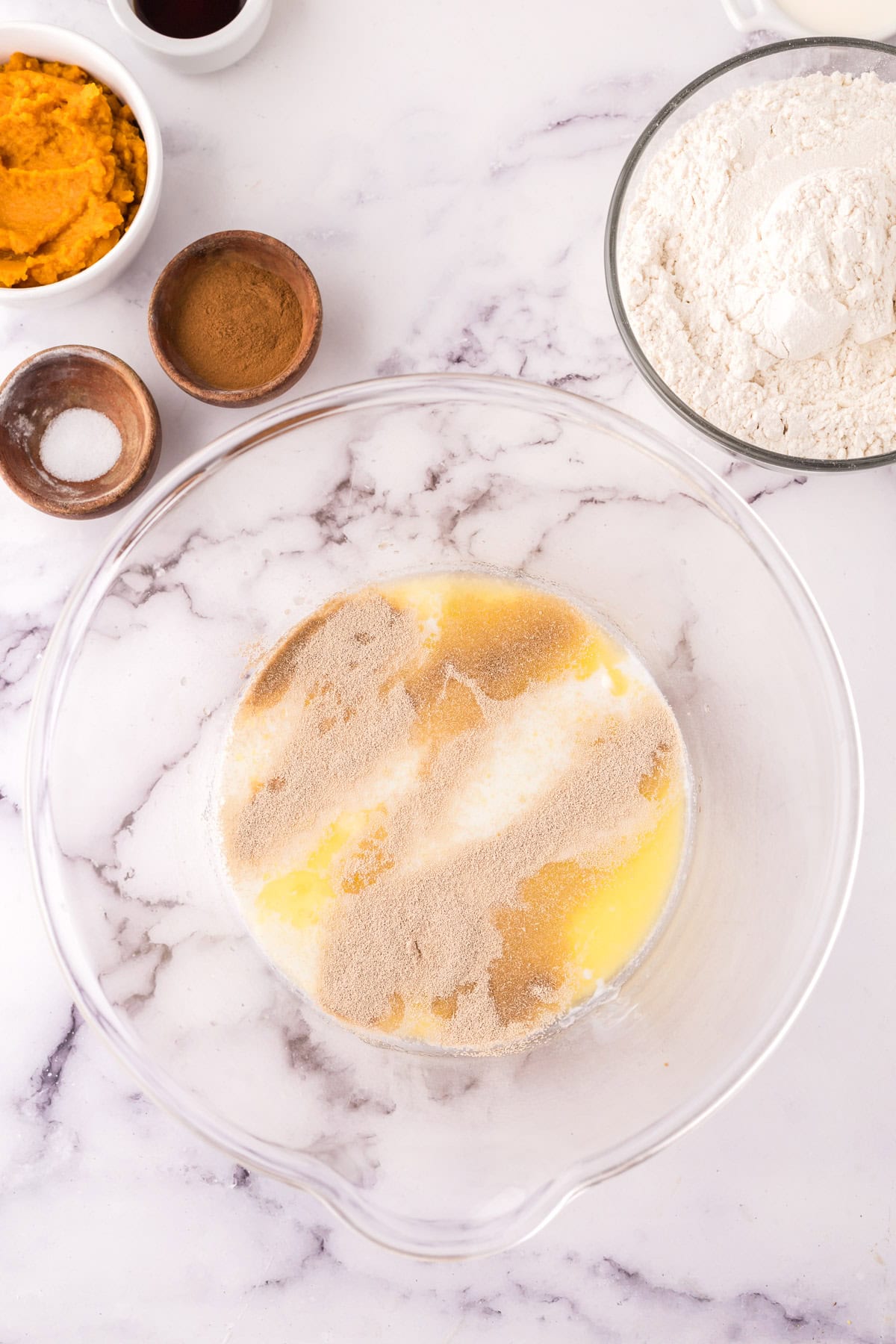 A glass bowl with milk, butter sugar, and yeast.