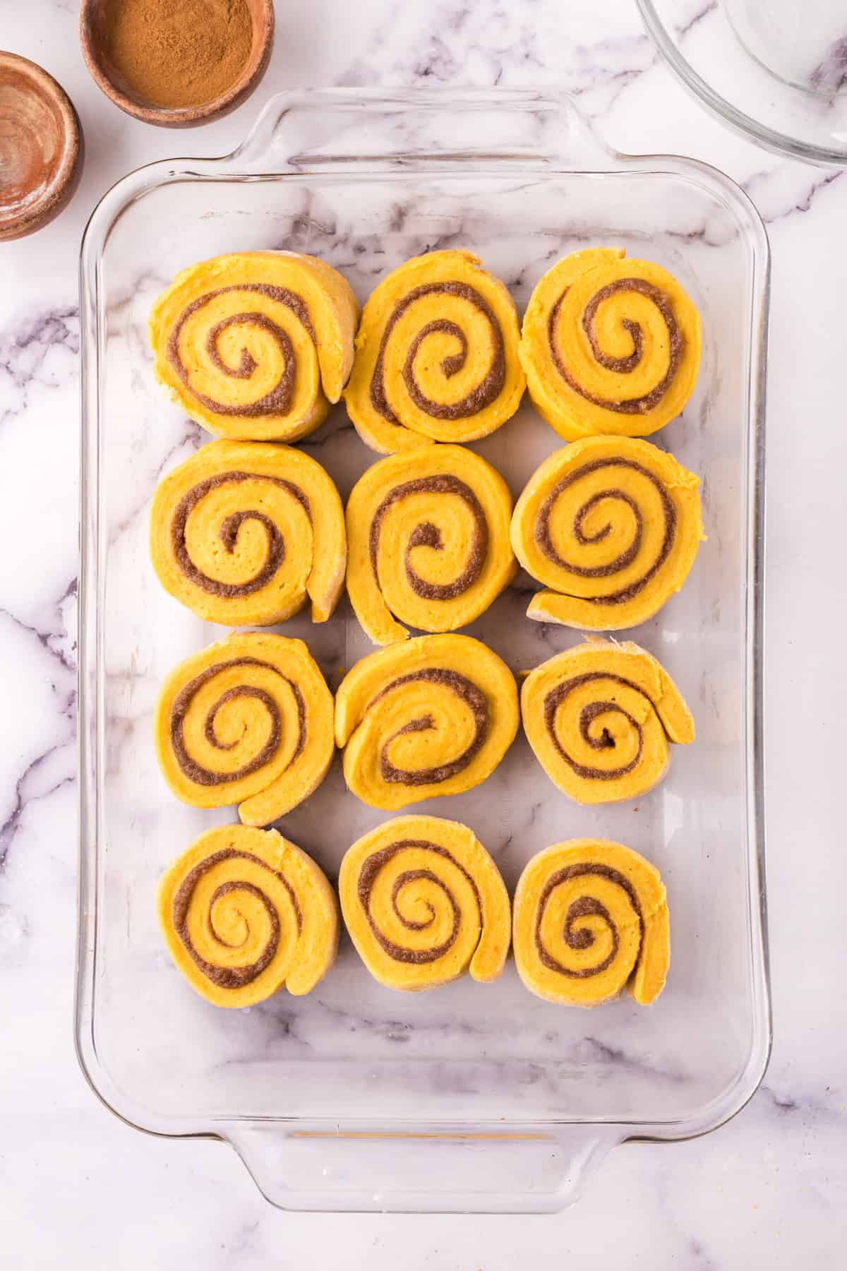 Uncooked pumpkin cinnamon rolls on a baking dish.