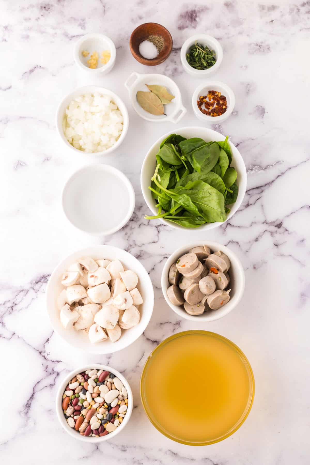 portion bowls each with raw ingredients to make sausage bean soup with spinach.