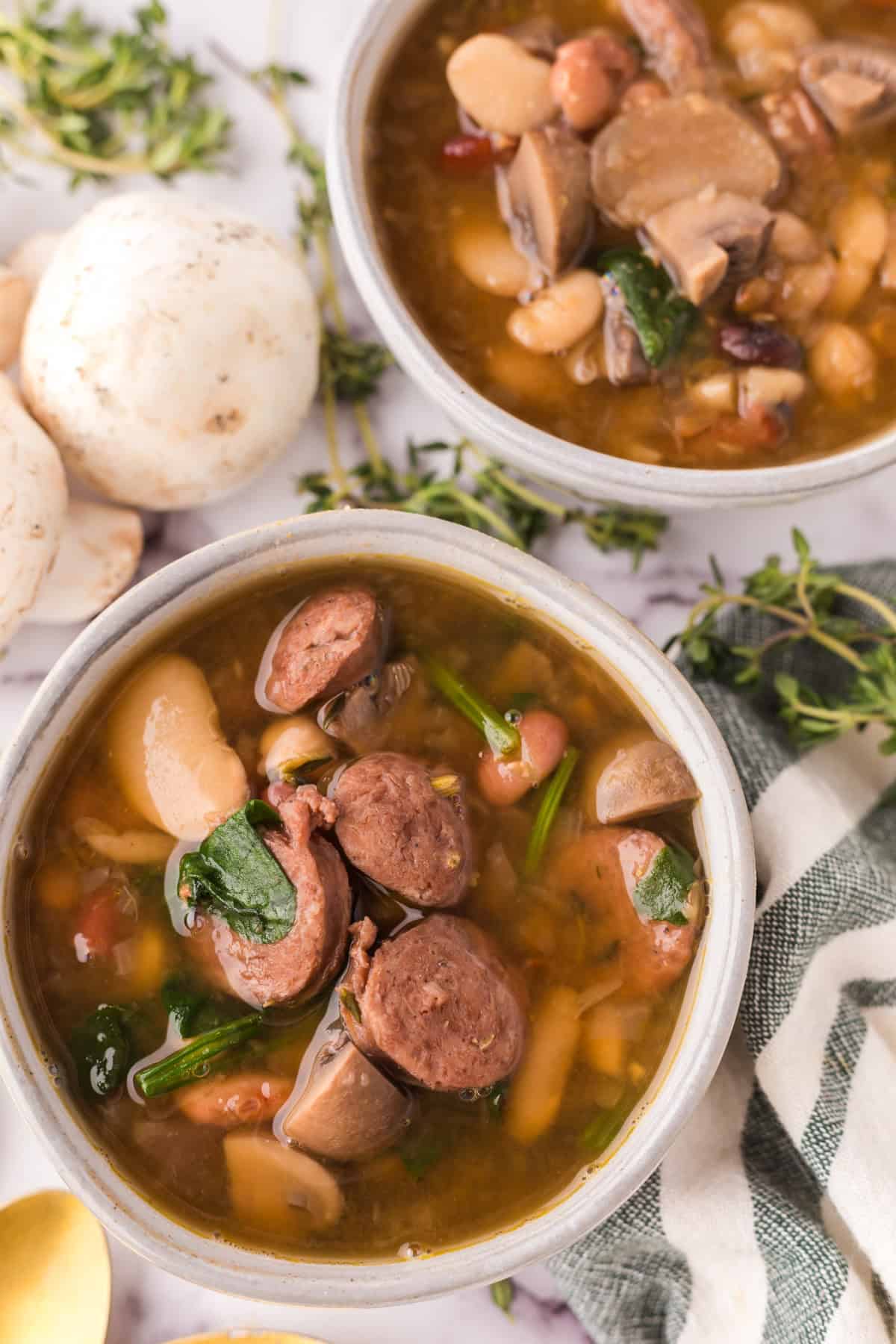 Sausage bean soup with spinach in white serving bowls.