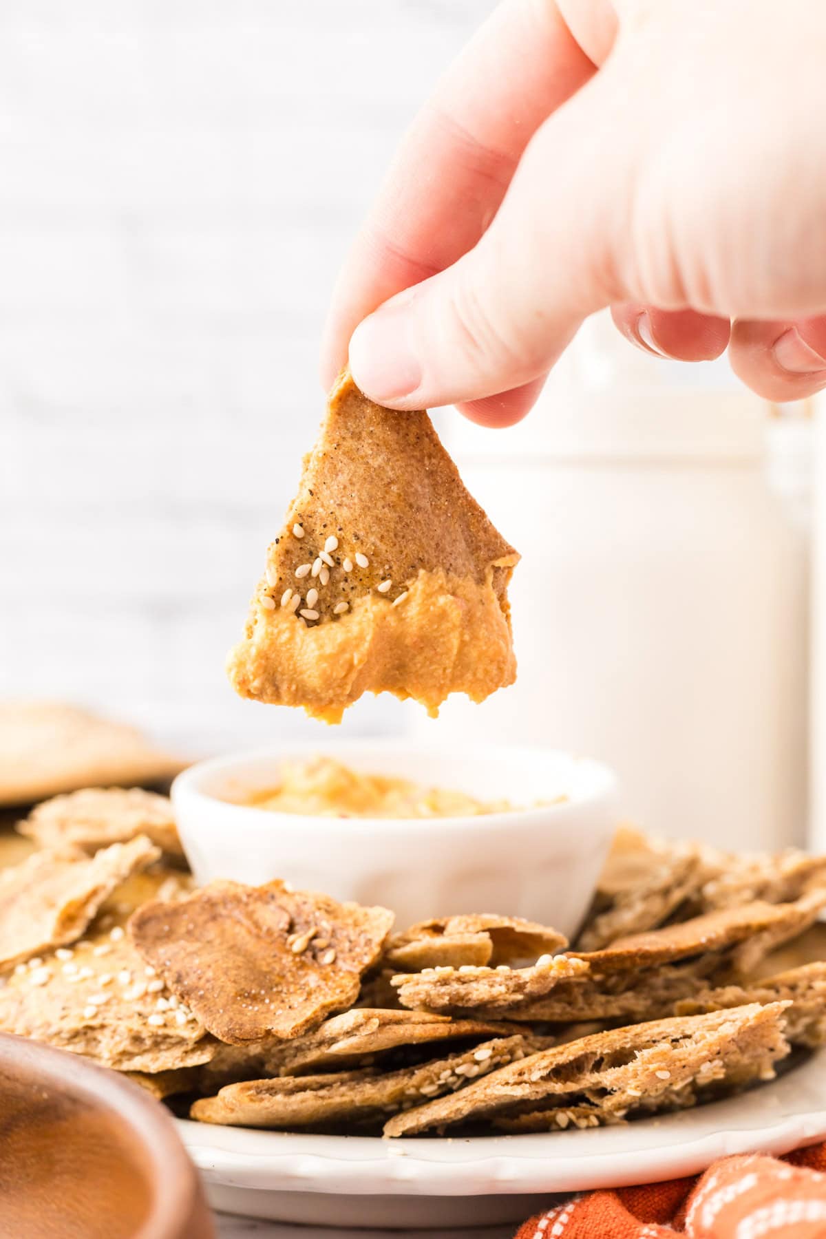 POV hand dipping simple lavish bread crackers on a round plate with a bowl of dip in the middle.