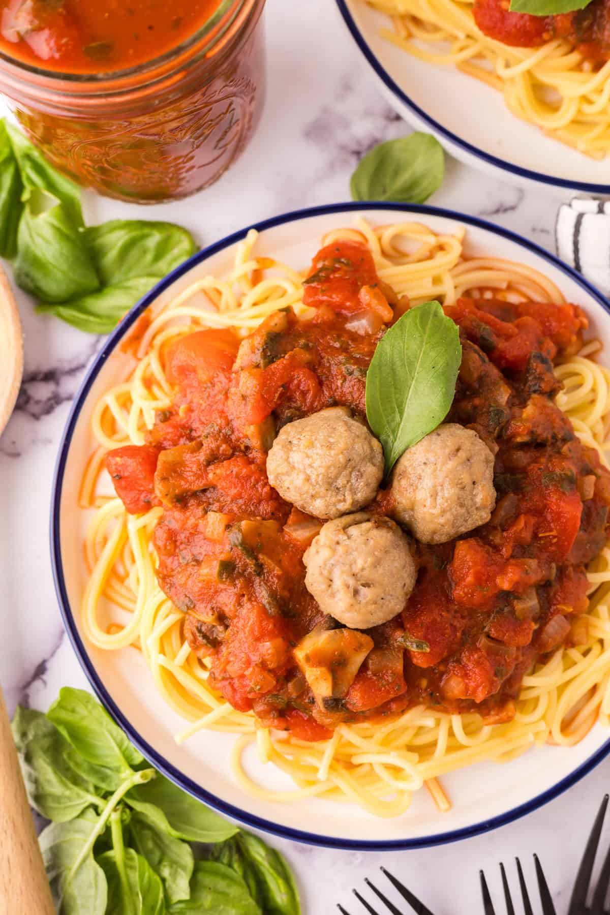 spinach mushroom marinara on a round plate of pasta with meatballs on top.