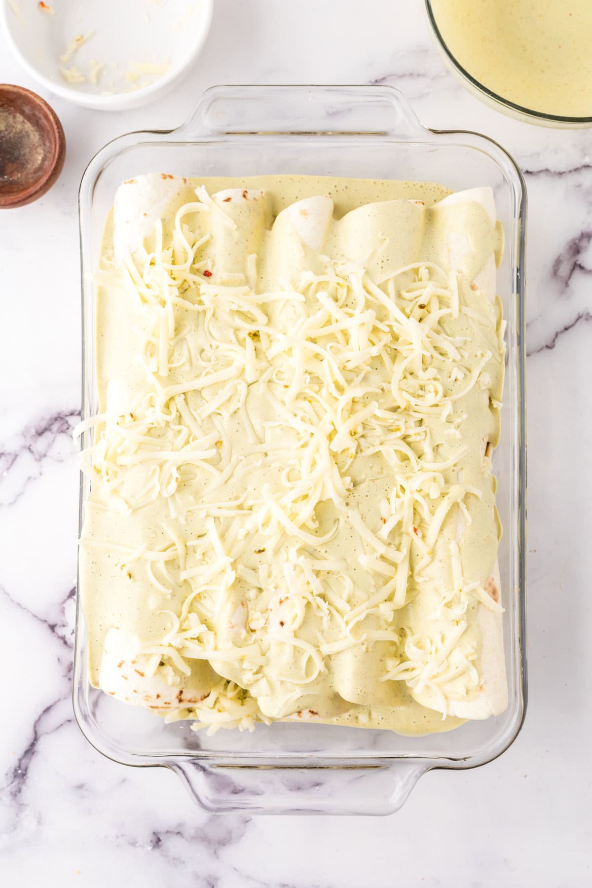 unbaked cheesy and gooey tomatillo ranch burritos in a clear casserole dish.