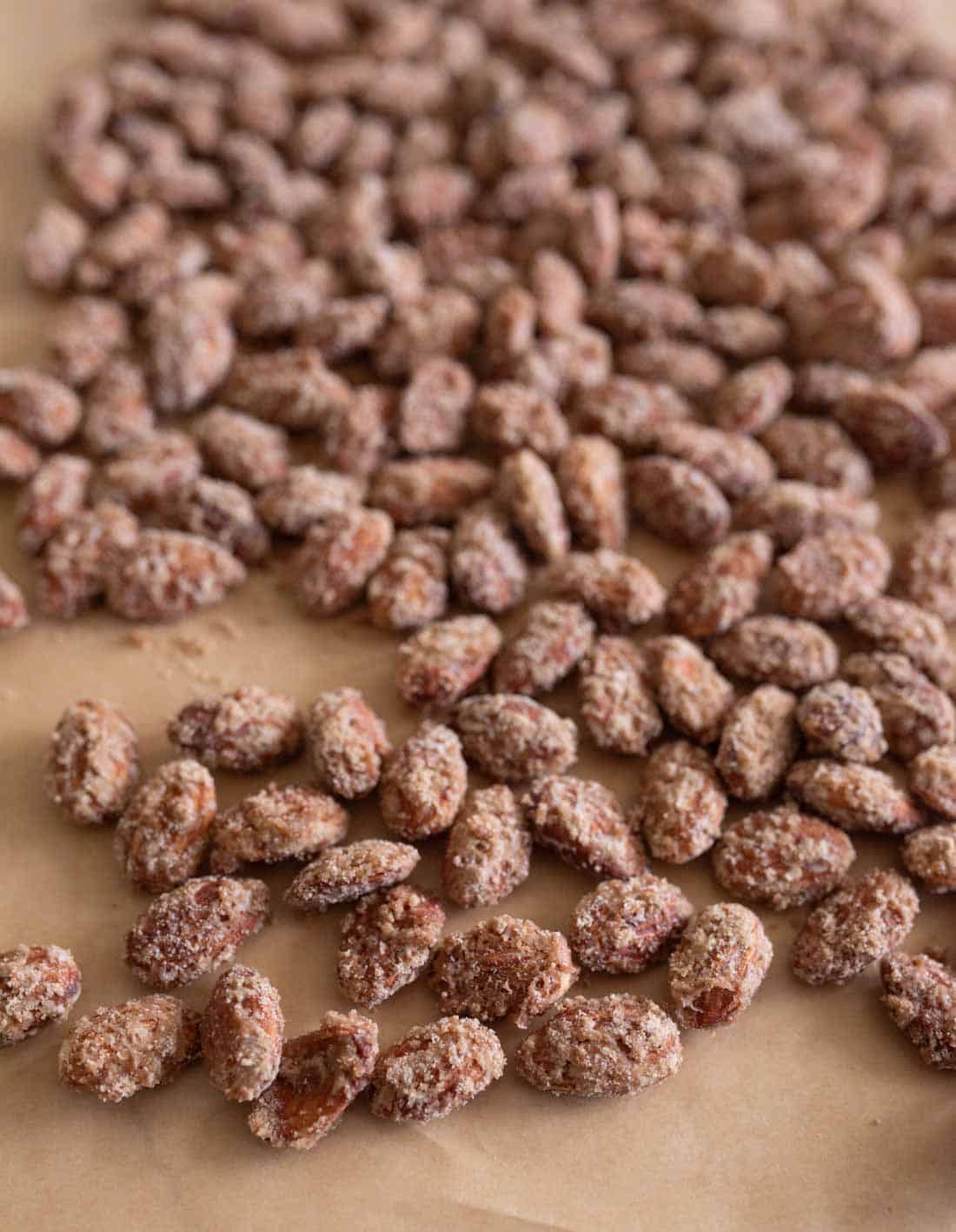 A close-up of roasted almonds coated with a layer of sugar and spices, spread out on a sheet of brown parchment paper.