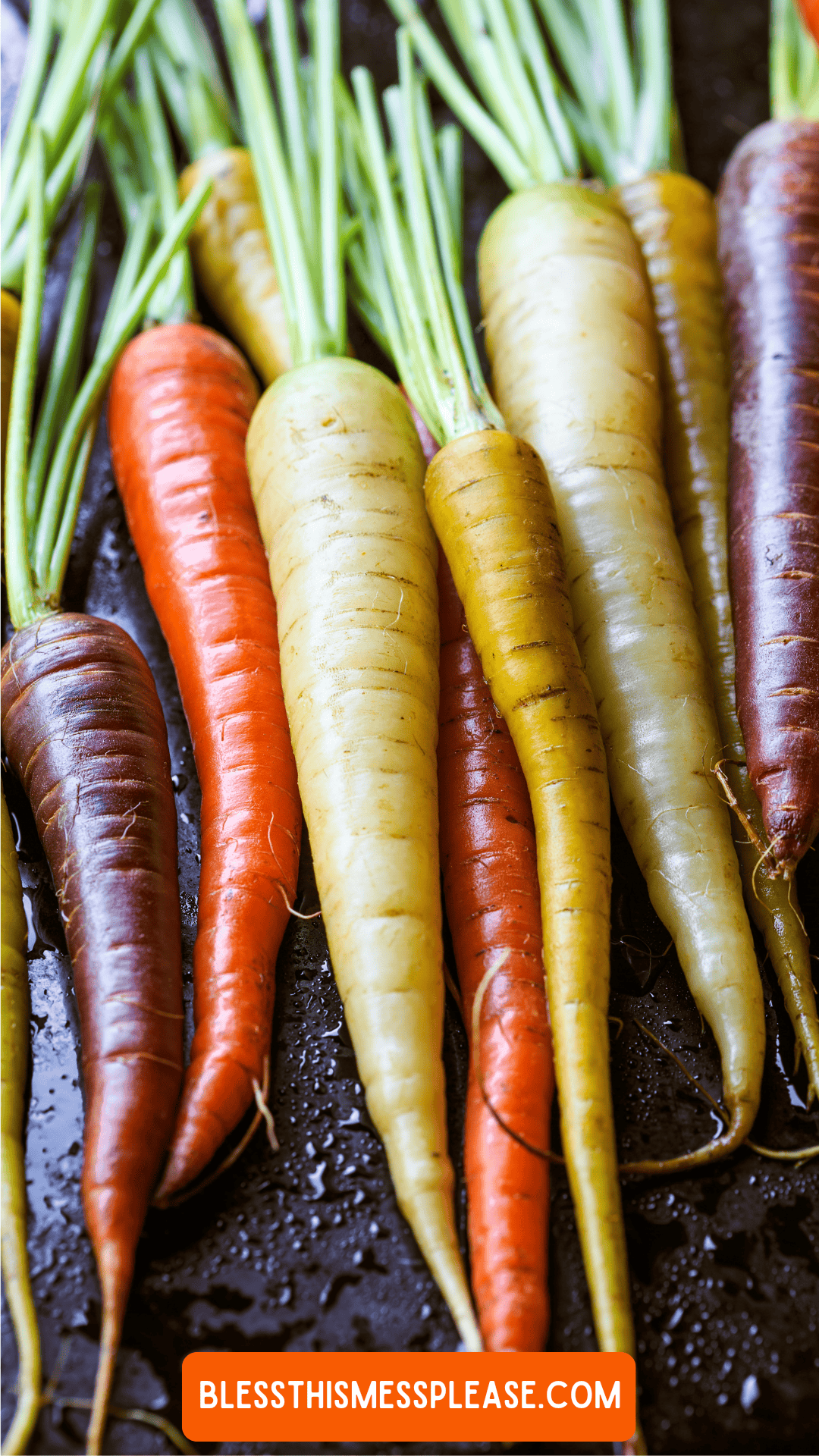 A close-up of colorful carrots, including orange, yellow, purple, and white varieties, with green tops attached. The surface appears wet and shiny. A label at the bottom reads