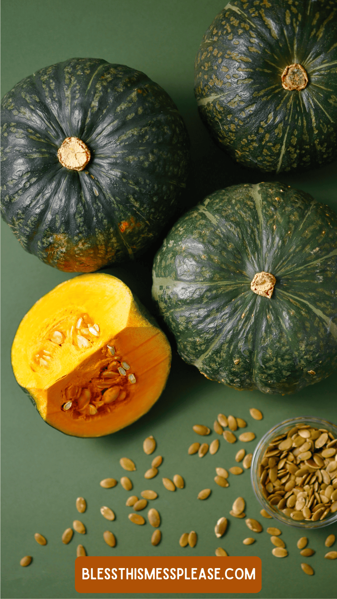 Three whole green kabocha squash, one cut open to reveal yellow flesh and seeds, with a small bowl of pumpkin seeds nearby on a green surface. Learn how to preserve winter squash at