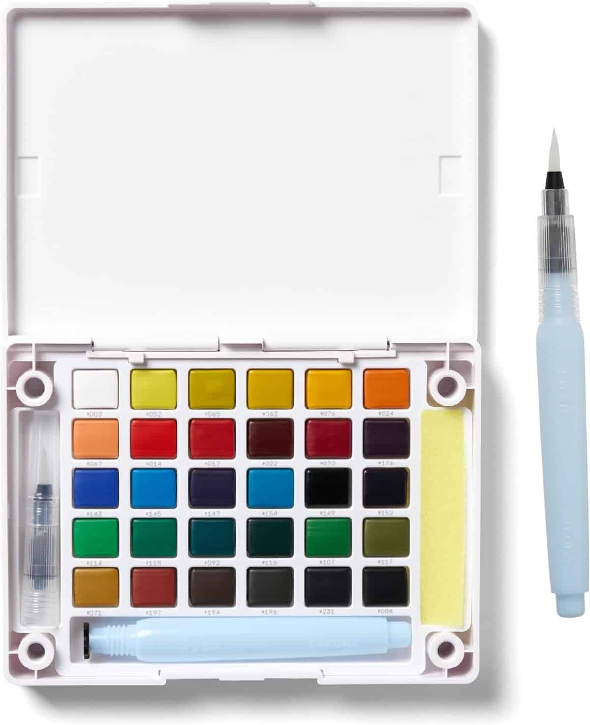 An open watercolor paint set with 24 colorful paint pans, a water brush pen, a sponge, and a water container pen inside a white plastic case. Another brush pen is placed to the right of the case.