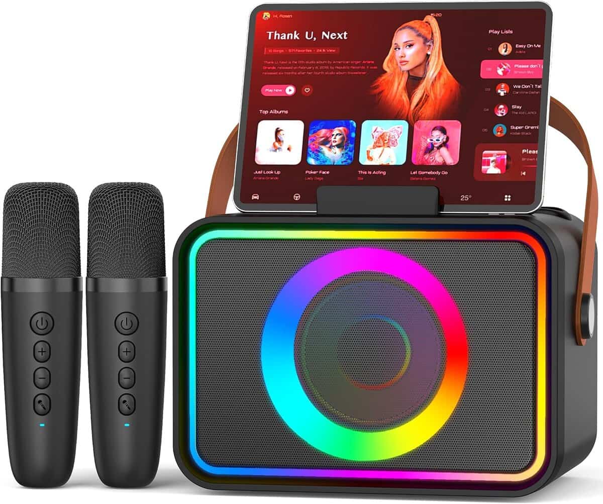 A portable karaoke machine with colorful LED lights, a tablet displaying a music playlist on top, and two wireless microphones placed beside it.