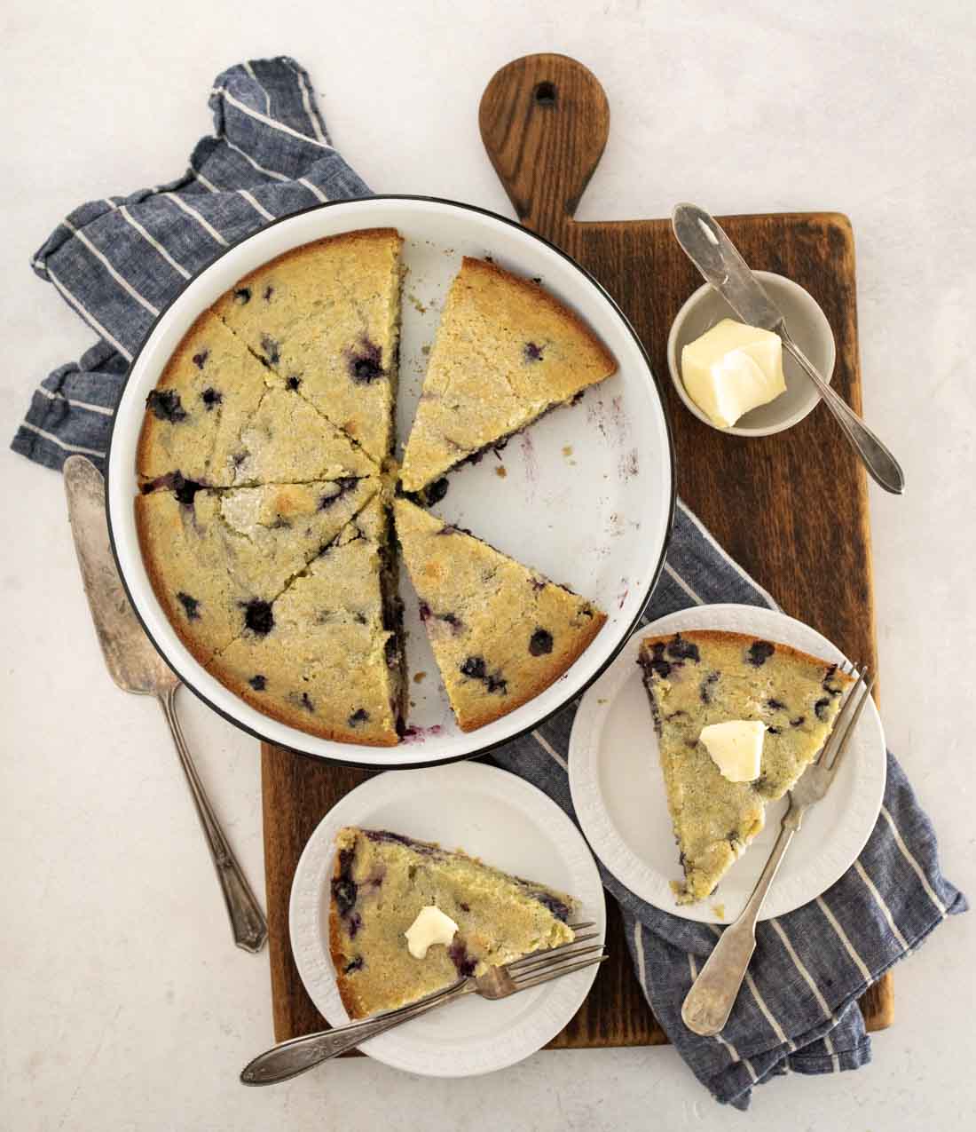 A plate of blueberry cornbread cake with butter sits on a wooden board.